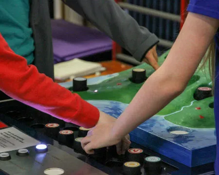 The arms of 3 different people selecting cylinders representing different types of energy source to place on an interactive exhibit map.