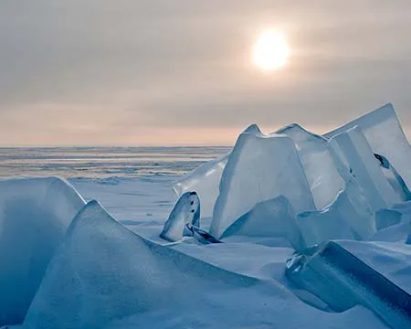 Shards of ice rise up from a frozen lake towards the hazy sunshine piercing the sky