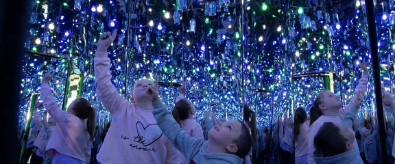 Children point upwards towards the shiny mirrored surface of the interior of the Every Can Counts exhibit