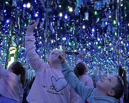 Children point upwards towards the shiny mirrored surface of the interior of the Every Can Counts exhibit