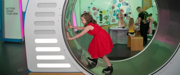A girl in a red dress walking in a giant hamster wheel