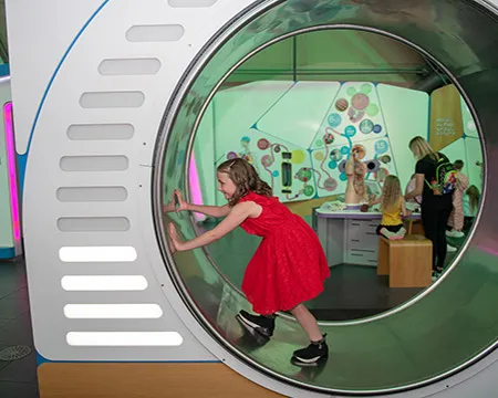 A girl in a red dress walking in a giant hamster wheel