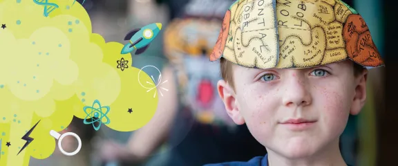 A young person wearing a paper hat showing the various parts of the brain smiles at the camera