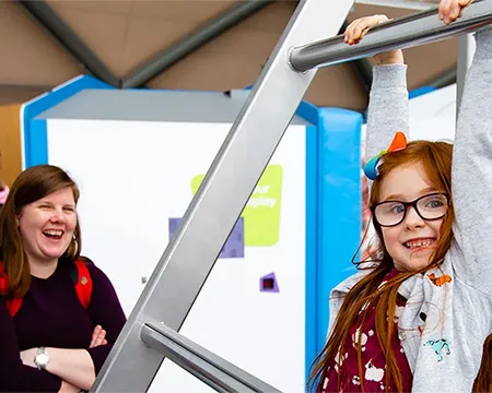 A young girl hangs on from a metal bar at an interactive exhibit