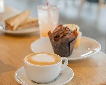 A coffee, cakes, and sandwiches on a wooden tabletop.