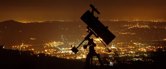 A telescope in silhouette above a city at night