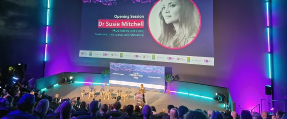 A speaker at the on-stage podium in front of the huge screen and a seated audience in the IMAX. Image: CAN DO Fest 2023