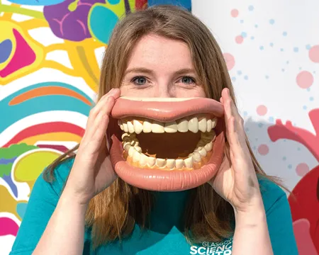 a science communicator holds a giant model of a mouth to their face