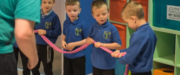 A line of school pupils hold a length of pink tubing to represent the process of digestion