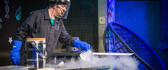 Our Amazing Air science show - a science communicator wearing safety gear pours out a beaker of liquid nitrogen