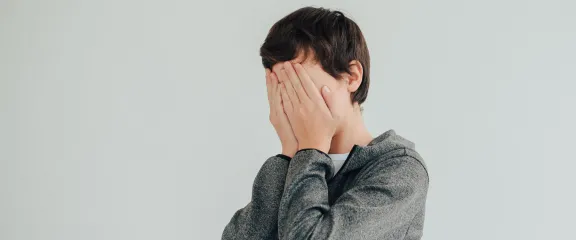 A young person holds their hands up to their face in embarrassment