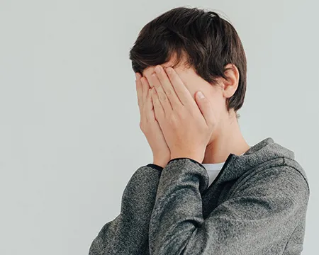 A young person holds their hands up to their face in embarrassment