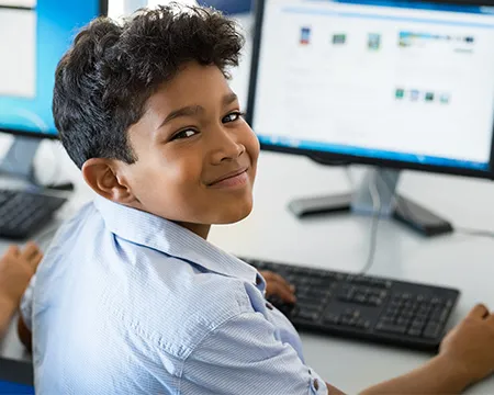 A happy schoolboy working on a desktop computer