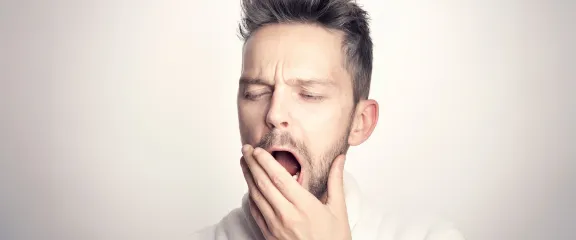 A yawning man raises his hand to his open mouth