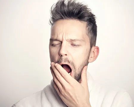 A yawning man raises his hand to his open mouth