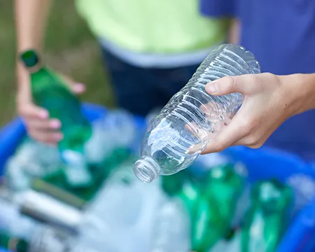Plastic bottles being placed into a recycling bin full of plastic bottles