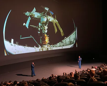 Two astronauts presenting an event using slides on the large screen