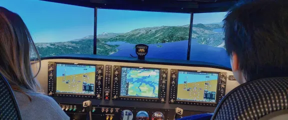 Two people at the controls of a flight simulator look out across a virtual landscape