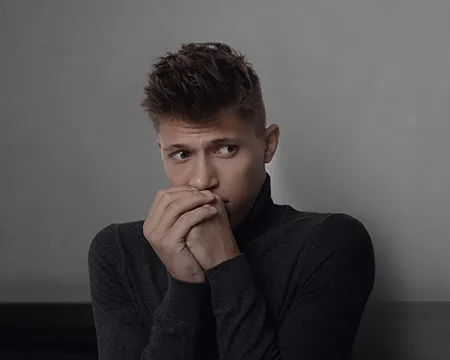 A man with hands clasped and raised to his face looks scared