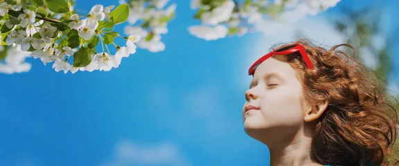 A girl smells the blossom of trees against the backdrop of a blue sky