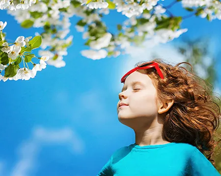 A girl smells the blossom of trees against the backdrop of a blue sky