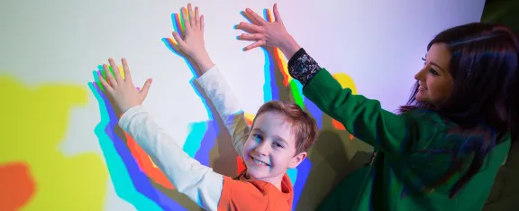 a child and an adult playing with the coloured shadows exhibit