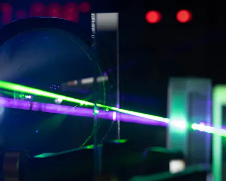 Green and purple beams of laser light passes through prisms in a photonics experiment