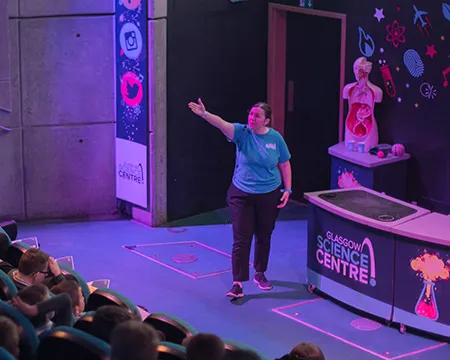 A presenter at Glasgow Science Centre gestures to an audience during a science show