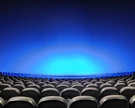 Empty cinema with rows of black seats facing a large screen illuminated in blue.