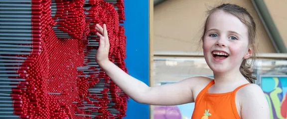 A child smiling whilst interacting with the pin wall exhibit
