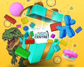 Open turquoise gift box with Glasgow Science Centre card; T‑rex, balloon dog, cake and colorful bricks bursting out.