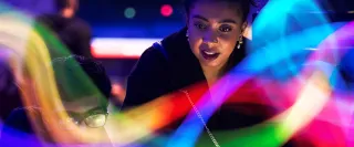 A woman and man gaze from the darkness through a colourful flow of light