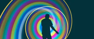 A person in silhouette is circled by a swirling rainbow of light