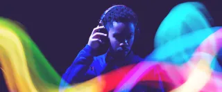 A man with headphones on behind a rainbow-coloured stylised light wave