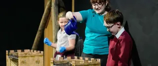 A presenter pours water onto a castle in a science show experiment