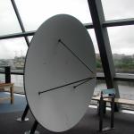 A white metal concave dish with three metal arms that meet at the focal point. One of the Whispering dishes - speaking quietly into the dish, a person at the second dish on the other side of the floor space would be able to hear what was being said.