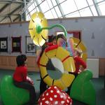 Young children explore large metal flower sculptures in the Alice in Wonderland exhibition