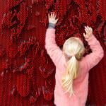 A young person reaches up and pushes against an array of red pins to make body shapes
