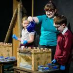 Science Communicator pours water onto a replica castle to demonstrate the strength of the roof