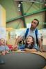 A family look up at a paper helicopter rising from a wind table.