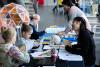 Children are creating colourful model brain hats at a table with experts