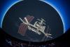 The International Space Station is projected up above the heads of The Planetarium audience and onto the domed ceiling. Behind the ISS are thousands of stars.