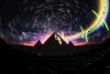 3 pyramids are in silhouette against a rich, starry backdrop in the planetarium. A rainbow runs in a strip around the circumference of the dome with the green band of light acting like a 'heartbeat'