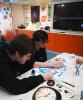 Two people at a workshop table working on their stained glass panels.