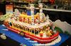 Colourful LEGO paddle-wheel riverboat with red, white and yellow trim, bunting, minifigures and blue studded "water".